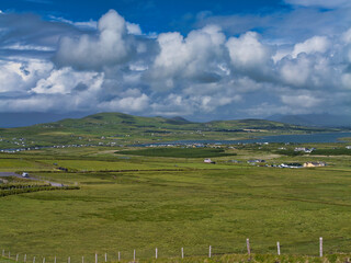 A panoramic view of rolling green fields and scattered cottages under a dramatic cloudy sky in Portmagee, Ireland.