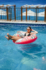 Woman Relaxing on Inflatable Ring in Swimming Pool Wearing Sunglasses