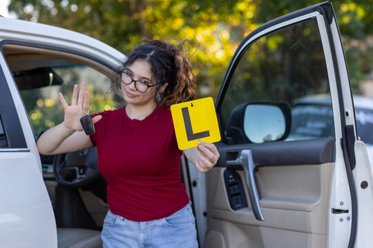 teenage girl holding up key fob and yellow L plate standing near a car