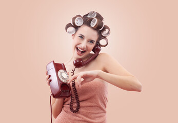 Portrait of a happy woman with hair curlers, using a vintage rotary telephone. Concept of hairstyle, makeup, beauty routine, and cosmetics. Possibly Making a hair appointment. Isolated on beige