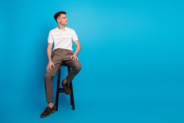 Young male sitting on stool in stylish casual attire against vibrant blue background