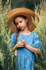 Portrait of a girl kid in a straw hat is standing in in a wheat field in summer.