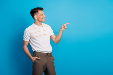 Confident young man pointing with enthusiasm against a vibrant blue background, showcasing elegance...