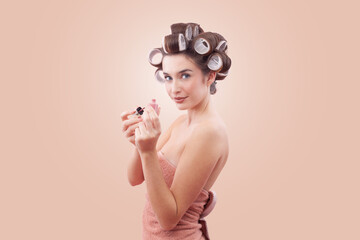 Young smiling woman with hair curlers applying nail polish while looking at the camera with her...