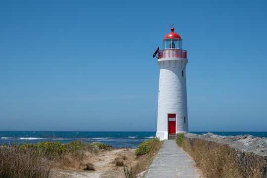 A pathway leading to a white lighthouse with a red top - Powered by Adobe