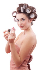 Young smiling woman with hair curlers applying nail polish while looking at the camera with her blue eyes. Concept of hairstyle, makeup, beauty routine, and cosmetics. Isolated on white background
