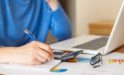 Businesswoman is working with financial documents, calculating and analyzing charts while taking...
