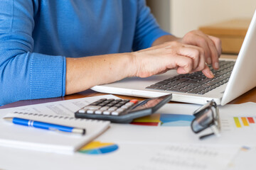 Businesswoman using laptop and analyzing financial charts, graphs, and data with calculator and...