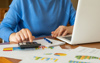 Businesswoman is working with financial data, using calculator and laptop, making calculations and...
