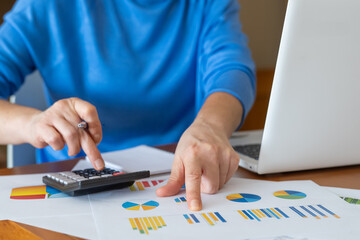 Businesswoman is working with financial documents, using calculator and pointing at charts while...
