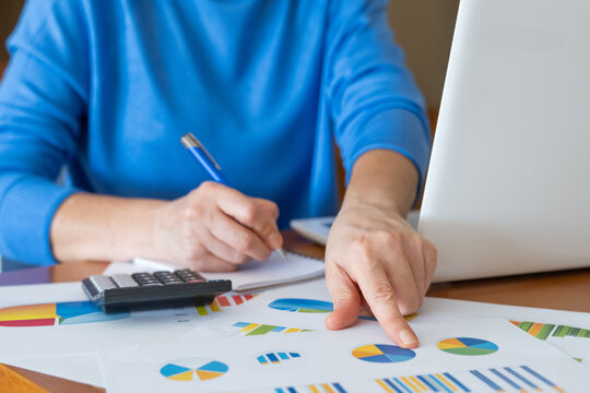 Businesswoman pointing at financial pie charts while taking notes in a notebook, developing investment strategy using calculator and laptop - Powered by Adobe