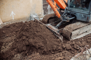 Tracked excavator pushes and levels a large pile of soil during site grading work for foundation construction at an urban jobsite.