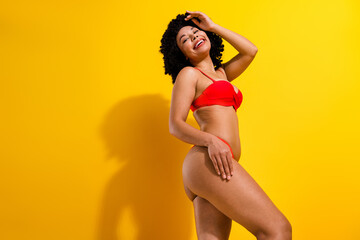 Confident woman in red swimwear posing against a vibrant yellow background exuding joy and style