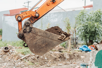 Close-up of an excavator bucket filled with dirt, lifting soil on a cleared urban lot prepared for...