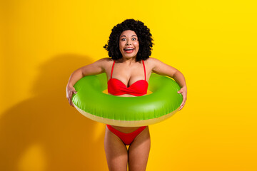 Vibrant Young Woman in Stylish Red Bikini Poses With Green Inflatable Against a Bright Yellow...