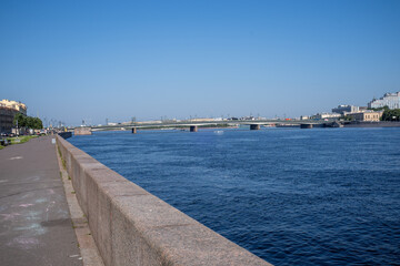 Obraz premium Granite embankment and bridge over a wide river in a sunny city.