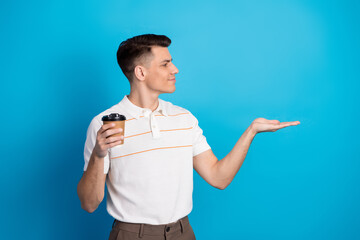 Young man in casual clothing holding a coffee cup with a welcoming gesture against a vibrant blue...