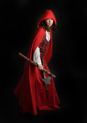 dramatic portrait of pretty young female brunette  model wearing a red hooded fairytale cloak and medieval historical gown. Holding a axe weapon. Isolated figure on dark studio background.