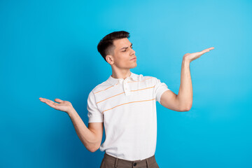Young man gesturing with both hands against a blue background, showcasing casual fashion and...