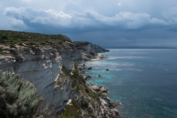 Fototapeta premium Impressive coastal cliffs in Corsica, France, rising above the Mediterranean Sea with dramatic light and textures. A rugged natural landscape shaped by sea and wind.
