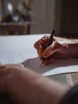 A person's hand holding a pen and writing on a lined notebook