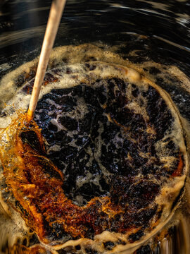 A dark liquid with frothy bubbles and swirls stirred with a wooden paddle