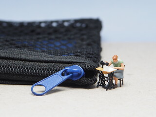 Mini toy of action figure at table with blurred background. Miniature photography concept design. Minifigure of tailor character with zipper. © awstoys