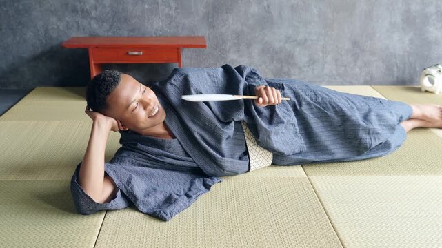 A black man wearing a yukata lying on a tatami mat to cool off