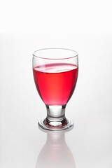 Glencairn type drinking glass containing bright red liquor, isolated on white background with reflection and bokeh