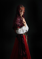 close up portrait of pretty young female brunette  model wearing a fairytale leaf mask and medieval historical gown. Isolated  moody figure on dark studio background.