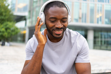 Music song concept. Good start day. Happy African American man listening modern hit on street in city. Person guy wearing headphones enjoy listening favorite music outdoor. People lifestyle joy
