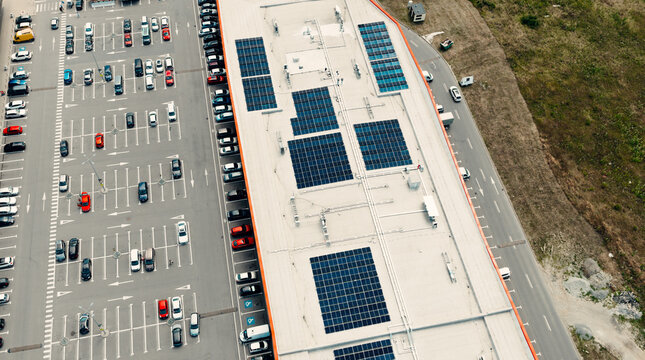 Solar panels providing green energy on commercial building roof with parking lot