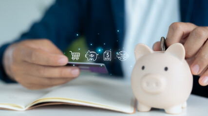 Close-up of hand holding credit card and saving coin into piggy bank with digital finance icons,...