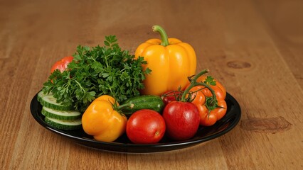 Colorful fresh vegetables arranged on a black platter. Detailed view of herbs, cucumbers, peppers, and tomatoes.