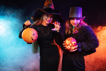 Two young woman wearing halloween costume witch on black background with magical colorful smoke...