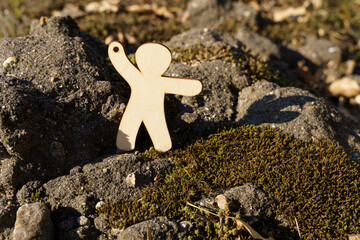 Wooden figure reaching out for assistance on a rocky surface in nature