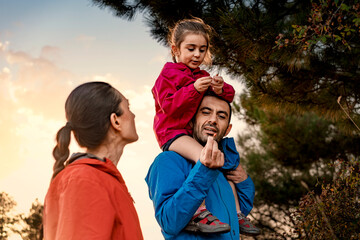 A father showing a wild berry to his daughter on his shoulders during a family hike. A parent...