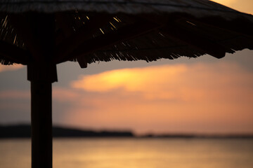 Sky with light clouds over the sea. In the foreground a bamboo sunshade. Sunset