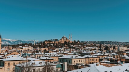 Wide-angle winter landscape highlighting snow-covered roofs, traditional mosques with tall minarets, and an imposing medieval fortress set beneath a vivid blue sky.