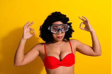 Beautiful woman wearing swim goggles posing confidently against a vibrant yellow background,...