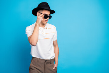 Young stylish man with sunglass and hat posing against a vibrant blue background, showcasing modern...