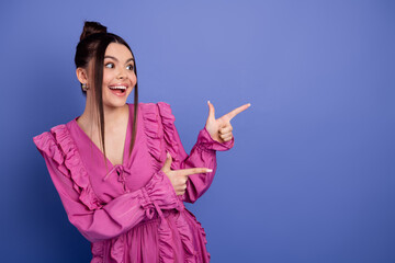 Young woman in a chic ruffled pink dress pointing with excitement against a vibrant purple...
