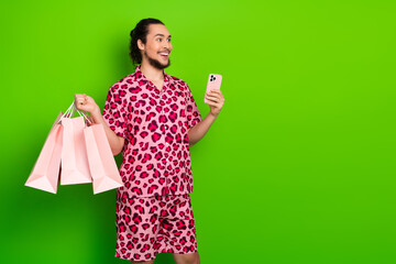 Young man in vibrant leopard print outfit holding shopping bags and a phone, standing against a...