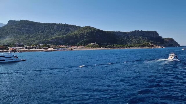 Seaside view to Kiris resort near Kemer, Turkey, with boats cruising on the deep blue Mediterranean Sea. Majestic Taurus mountain on the coastline background