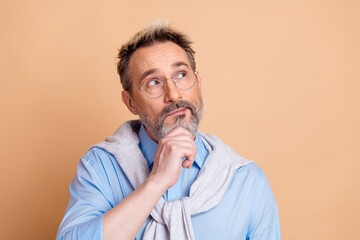 Mature businessman with calculated expression pondering thoughts against beige background in...