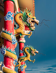 Intricately carved dragons adorn vibrant pillars under a cloudy sky