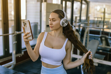 Portrait of young sportswoman with smartphone listening to music in gym.