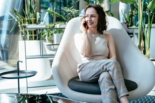 Woman in plaid trousers talking on phone in modern office chair