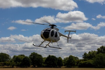 White helicopter flying over field with blue sky.