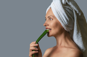 Side view happy woman, biting aloe vera leaf with white teeth on gray. Anti-aging care concept.